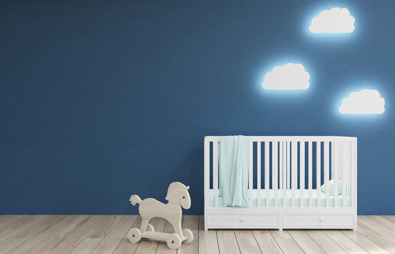 Cadrage sur une chambre d’enfant où se trouvent un lit de bébé, un cheval à bascule et des appliques murales en forme de nuages.