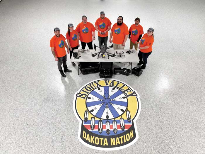 Groupe de personnes vêtues de chemises oranges devant un grand écusson portant le nom de Sioux Valley Dakota Nation