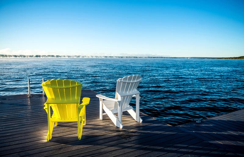 Deux fauteuils Muskoka sur une terrasse au bord d’un lac magnifique.