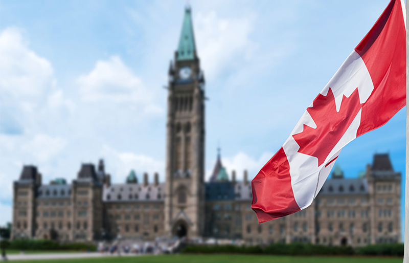 Cadrage sur un drapeau du Canada qui flotte devant le Parlement